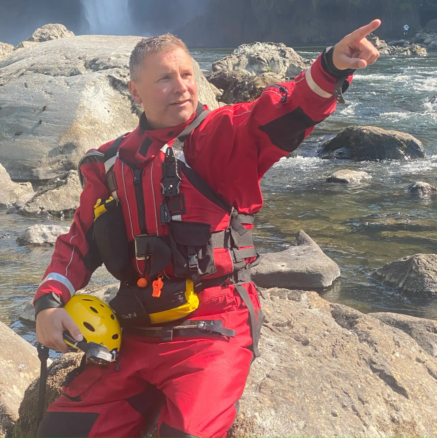 A man in red and black water suit pointing to the sky.