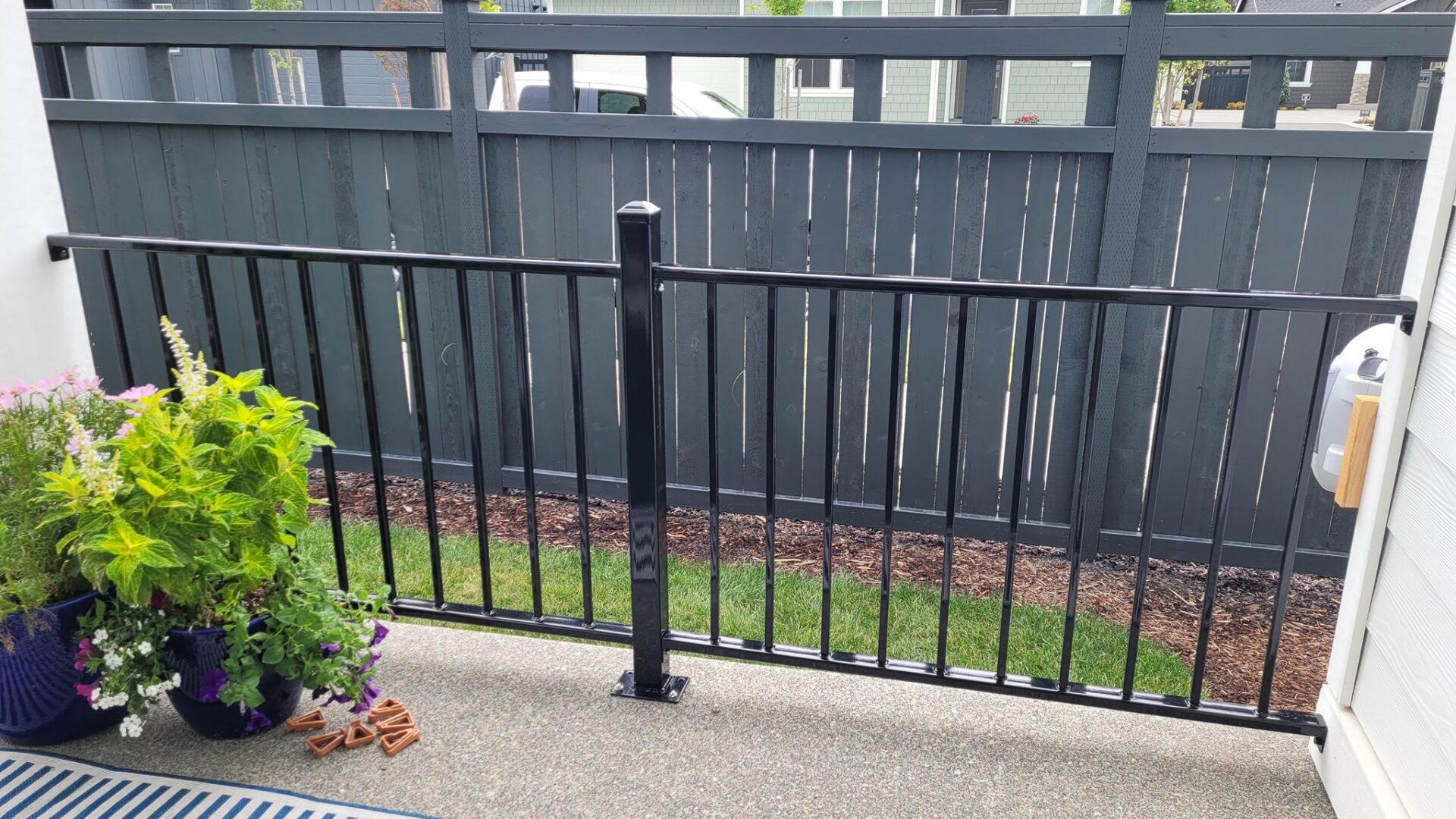 A black fence with a metal post and a green bush.