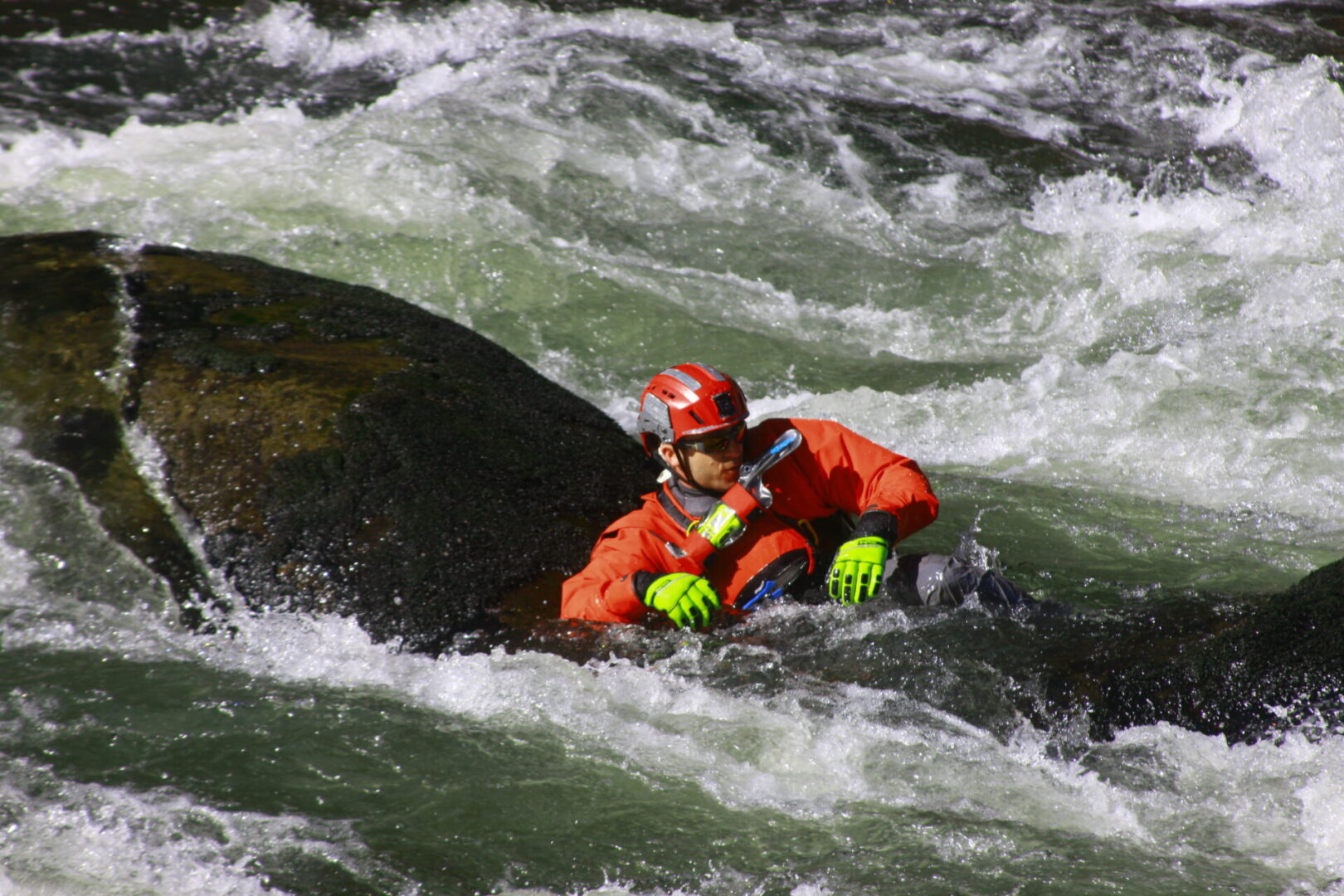 A man in orange jacket riding on top of rock.