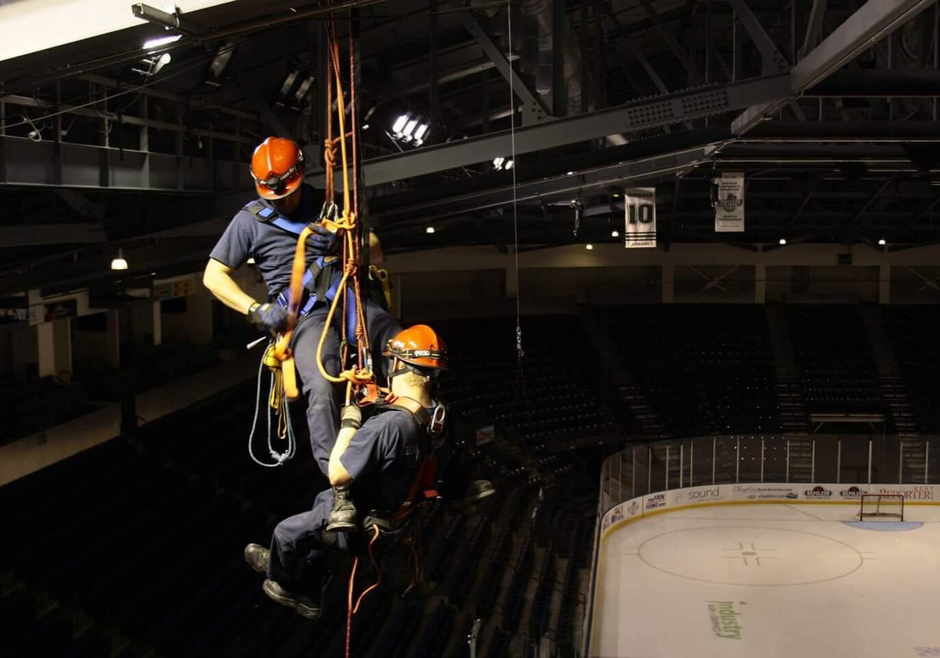 Two men in hard hats hanging from a rope.