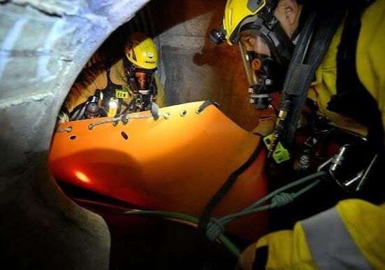 A man in yellow helmet and goggles working on an orange object.